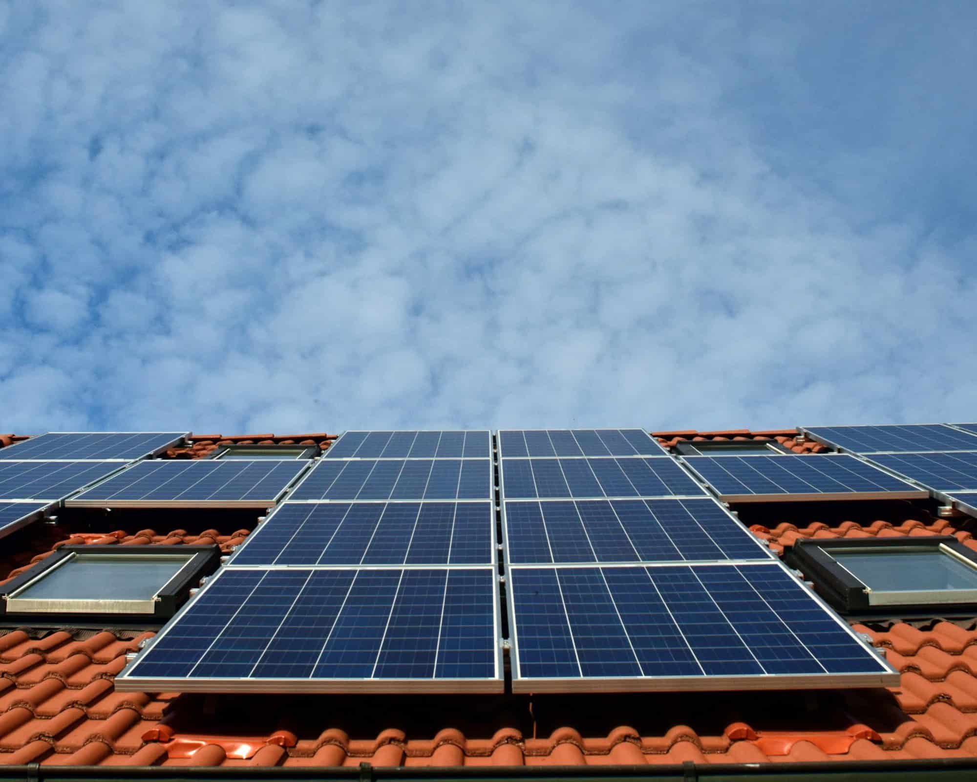 Photovoltaik-Module auf einem roten Ziegeldach unter blauem Himmel.