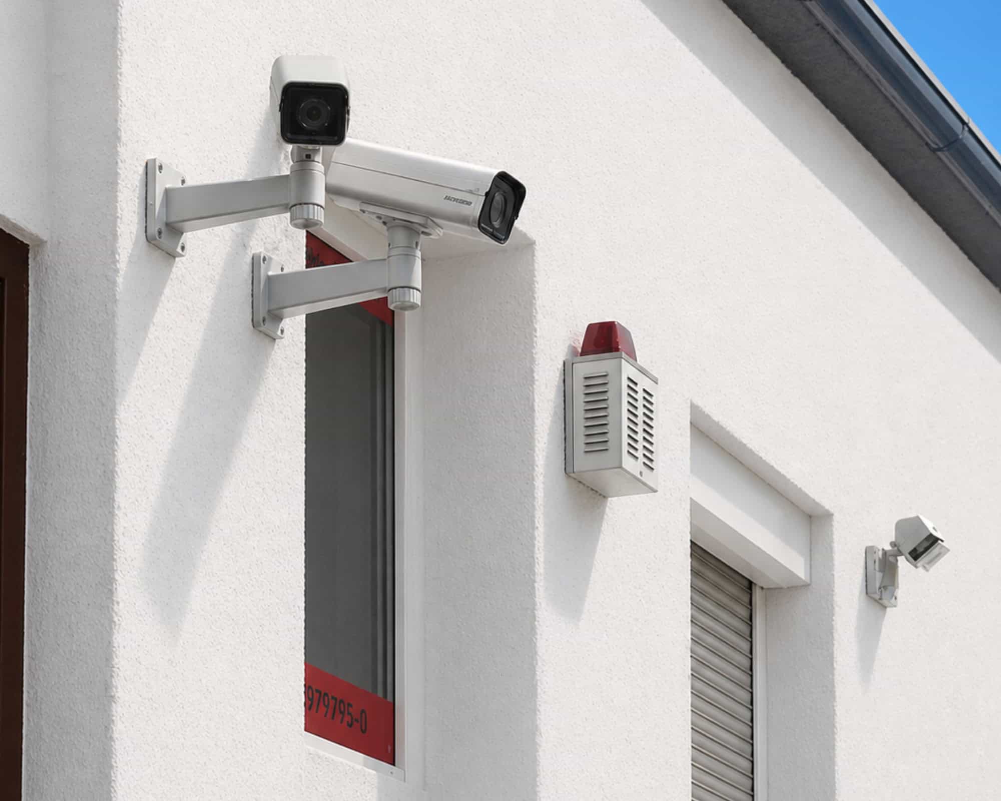 Überwachungskameras und Alarmsystem an einer weißen Hausfassade.